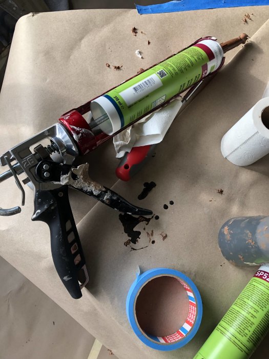 Använd fogpistol märkt Tajima Convoy med tom tub i en rörig arbetsmiljö, omgiven av spill och verktyg.