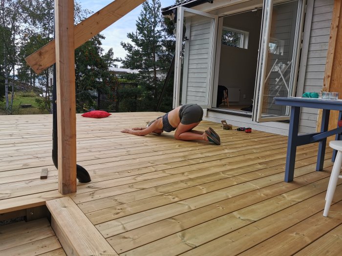 Person böjer sig framåt på en nybyggd trädäck altan, dörr till huset öppen, verktyg synliga.