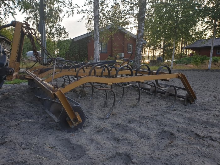 Gul traktorharv i arbete på ett nyligen bearbetat jordfält på landsbygden.