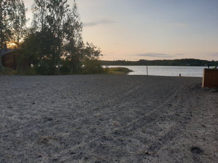 Solnedgång över ett nyligen harvat fält med luftig matjord nära en sjö på landsbygden.