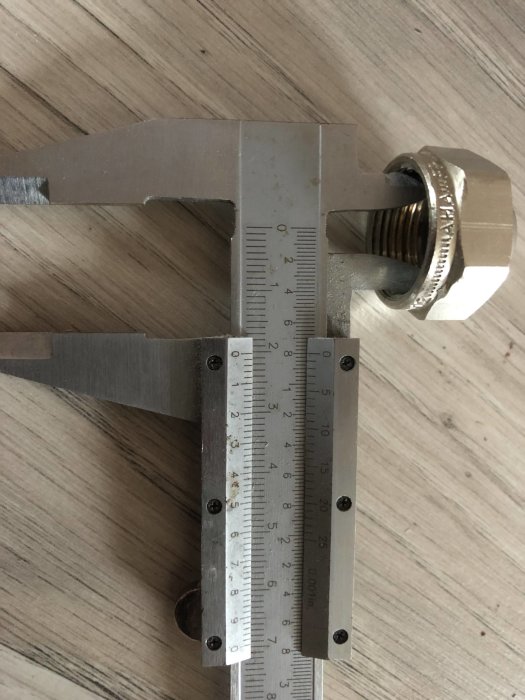 Mätskiva mäter invändig diameter på en rördel placerad på trägolv, visar nära 20mm mått.