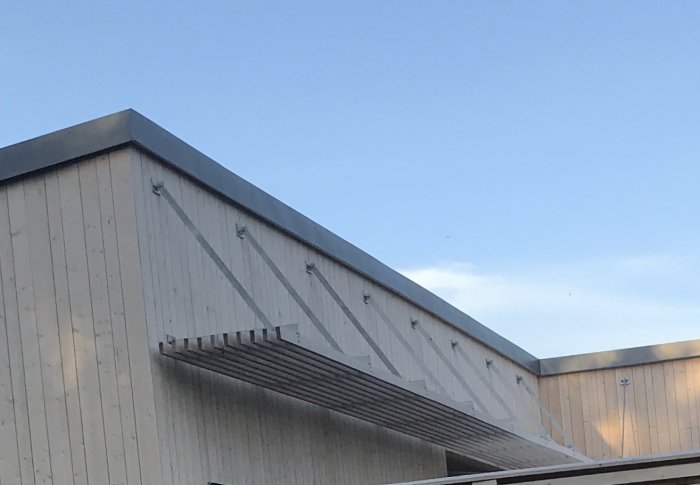 Träkonstruktion av ett pergolatak som är fäst vid husfasaden under en klar himmel.