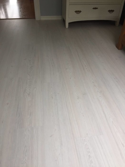 Matt Tundra-golv bredvid glansigare laminat i hallen, med synliga skarvar och vit byrå.