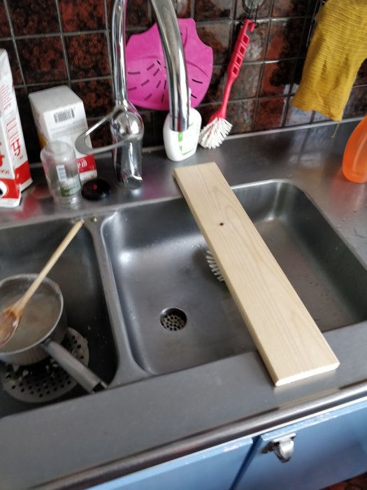 Träspillbit placerad på kanten av en rostfri diskbänk med en diskho och diverse diskredskap.