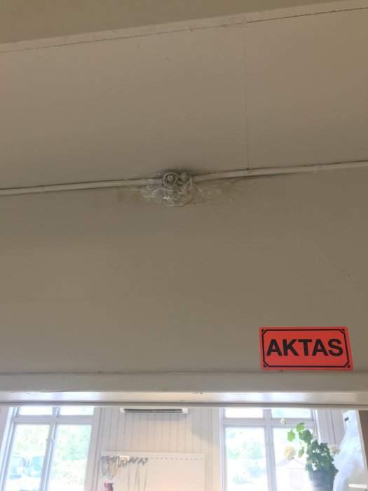 Porslinsdosa fästad på vägg med packtejp över skylt som säger "AKTAS", inomhusmiljö.