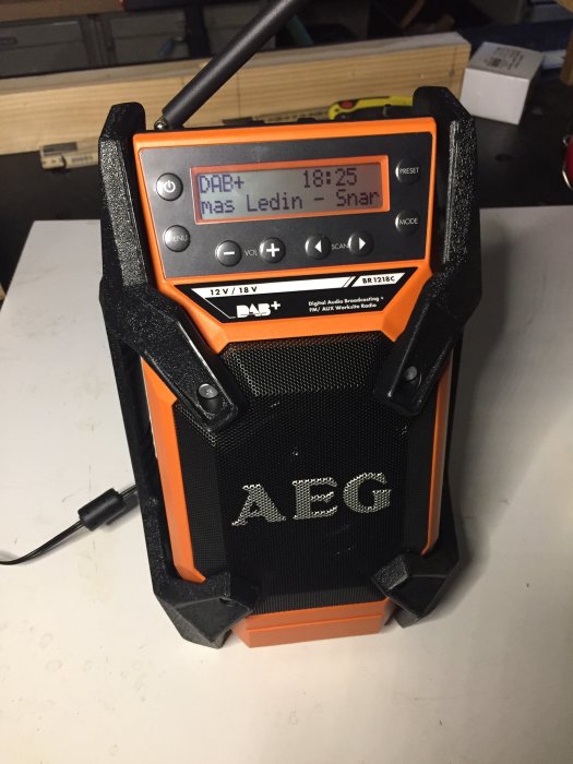 Orange svart arbetsradio från AEG visar DAB+ station och tid, används under byggprojekt.