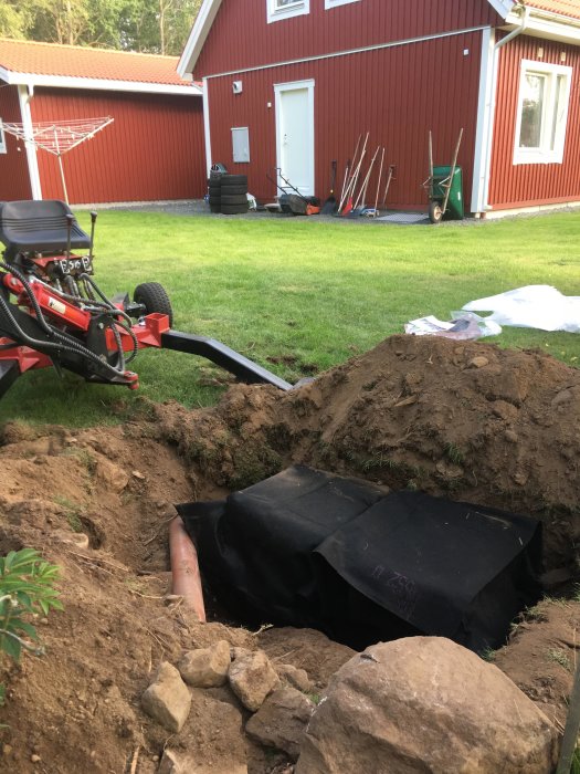 Nergrävda stenkistor för dagvatten vid garage med uppriven gräsmatta och trädgårdsredskap i bakgrunden.