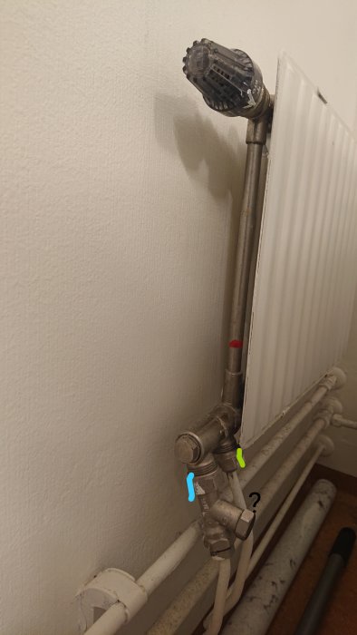 Radiator med termostat och anslutningsrör markerade med färg för att illustrera frågan om demontering.