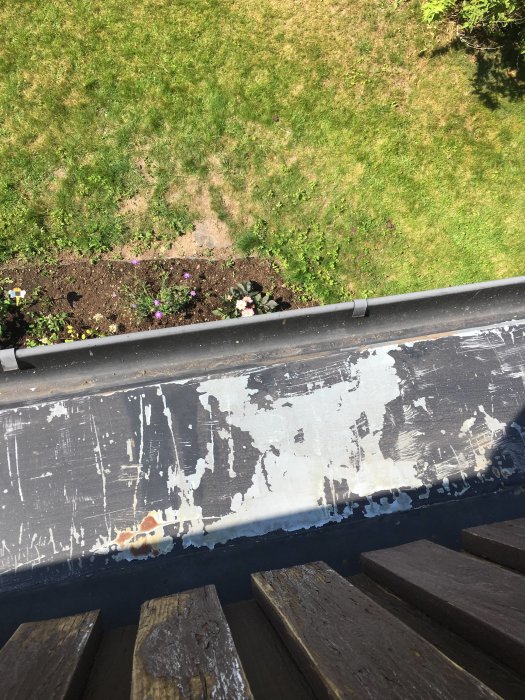 Närbild på ett slitet plåttak med flagande färg och synlig rost, sett från en veranda med trägolv.