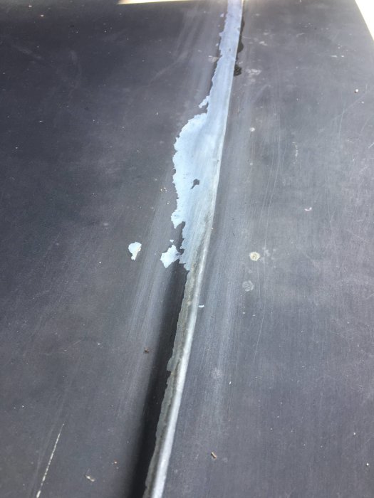 Flagnande färg på svart plåttak med synlig underliggande metall.