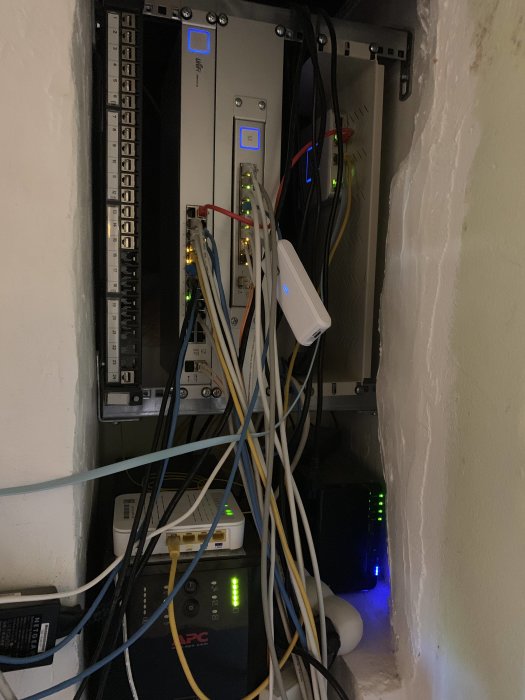 Nätverksutrustning i serverrum med patchpanel, switchar, UPS och diverse kablar.