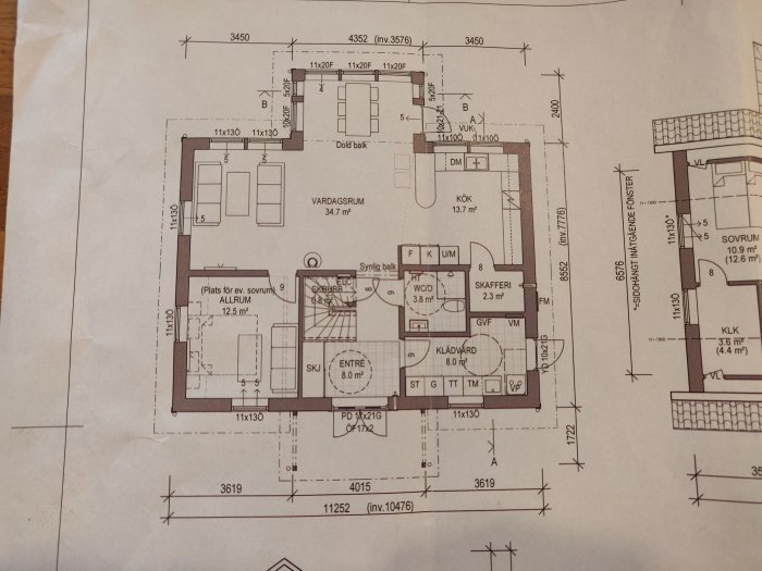 Pappersritning av planlösningen för ett hus med markerade rum som kök och vardagsrum samt måttangivelser.