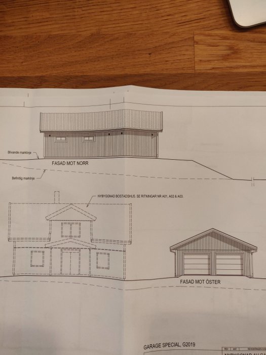 Arkitektritningar av ett hus och ett garage sett från olika väderstreck på ett bord.
