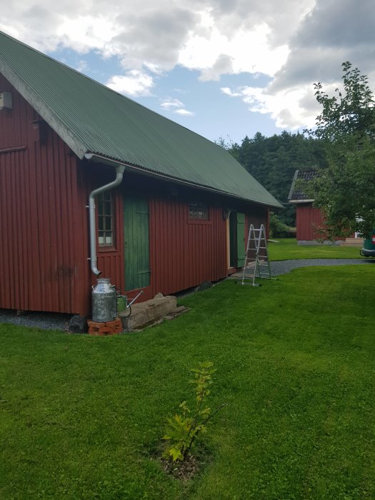 Röd träbyggnad med nyjusterad takränna och stege, omgiven av grön gräsmatta.