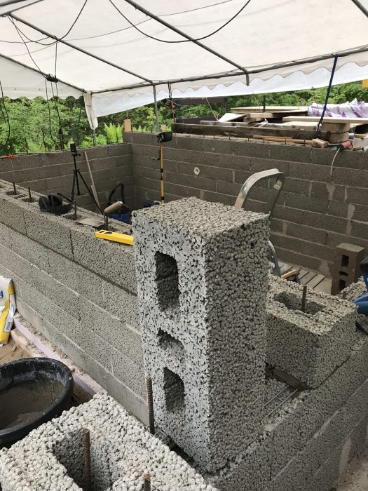 Pågående byggnation under ett tält med den sista lagda betongstenen i en mur.