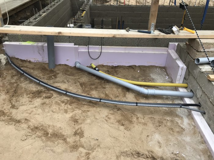 Elledningar och rörinstallationer mot en källarvägg i ett byggprojekt.