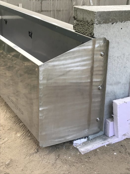 Rostfri behållare installerad i byggarbetsmiljö, exakt precision nära betongkant, förberedd för liner.