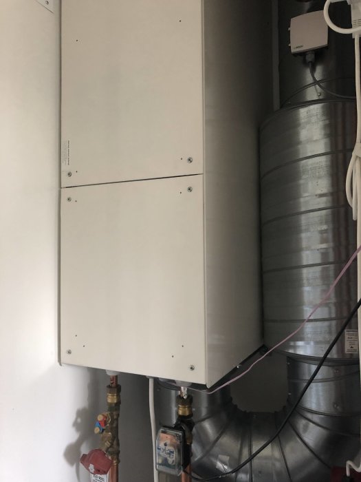 Ventilationssystem med vit frontpanel och synliga anslutningsrör samt elinstallationer.