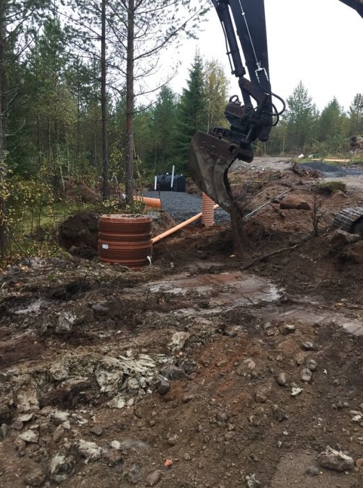 Grävmaskin vid arbete med grävning och installation av brunnsringar och rör i skogsmiljö.
