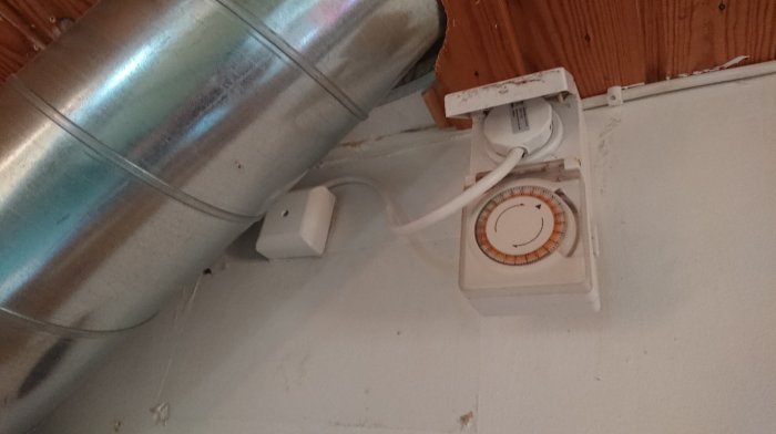 Elektrisk timer och stickkontakt på vägg, ansluten med synlig kabel och dosa.