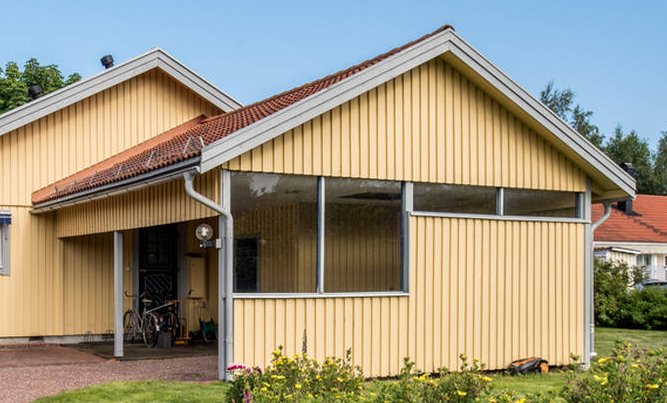 Gul villa med angränsande dubbel carport med tegeltak, snörasskydd och tre väggar, ingen betongplatta synlig.