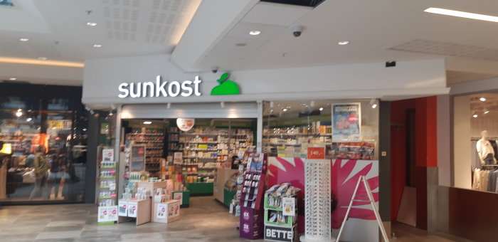 Entrén till en Sunkost hälsokostbutik i ett norskt köpcenter med skyltfönster och diverse produkter.