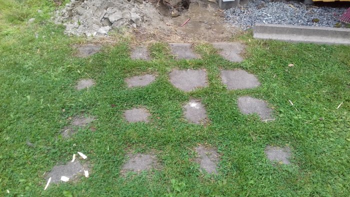 Gammal grästäckt stenplattor på en gräsmatta redo att tas bort för att användas vid en ny farstukvist.