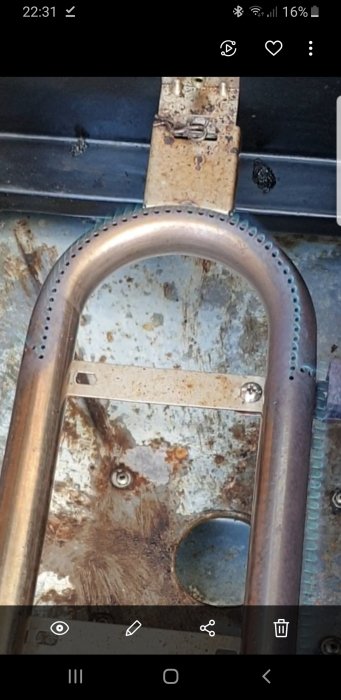 Närbild på en brännare med små hål längs kanterna mot en rostig metallbakgrund.