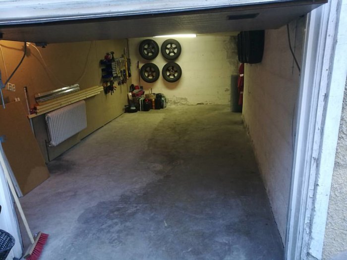 Ett garage med nyligen gjutet och dränerat golv, verktygshängare och bilhjul på väggen.