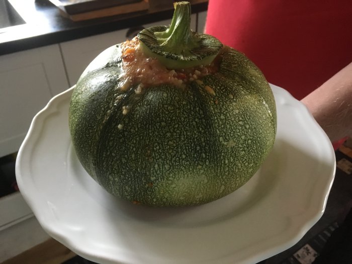 Fylld squash med köttfärs och bulgur på en tallrik som någon håller i.