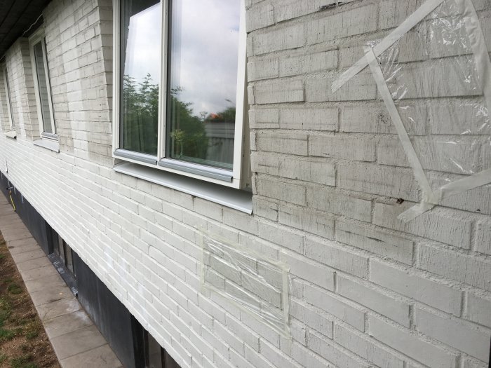 Målad tegelfasad med plastfolie för fukttest efter tvättning.