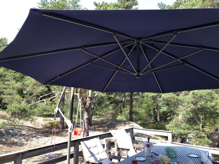 Blått parasoll på träaltan med utsikt över skog och klippor i bakgrunden.