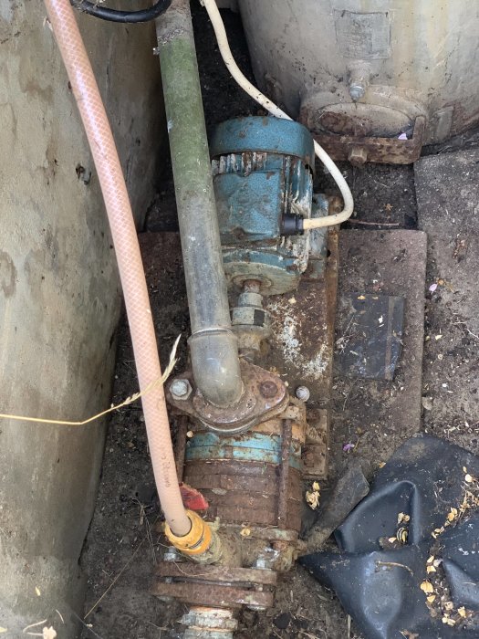 Gammal rostig vattenpump och tank i brunnen för bevattning.