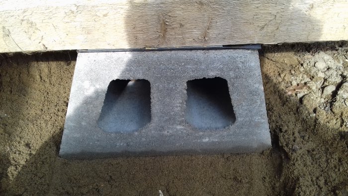 Stenplatta under träregel med plåt och papp mellan, använd i byggprojekt för att förhindra fukt.