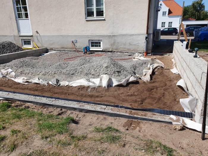 Byggplats med grus och dräneringsrör vid husgrund, påbörjad markarbeten för renovering.