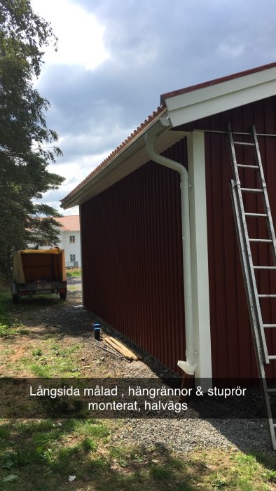 Nymålad byggnadslångsida med nyinstallerade stuprör och hängrännor, grus och stenar i förgrunden.