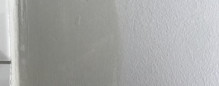 Nyligen spacklade och målad grå vägg med tydlig nyansskillnad där spacklet applicerats.