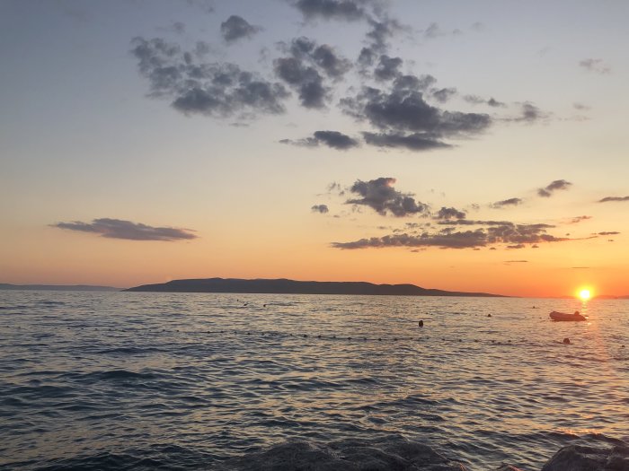 Solnedgång över havet med bergssiluett i bakgrunden och små båtar på vattnet.