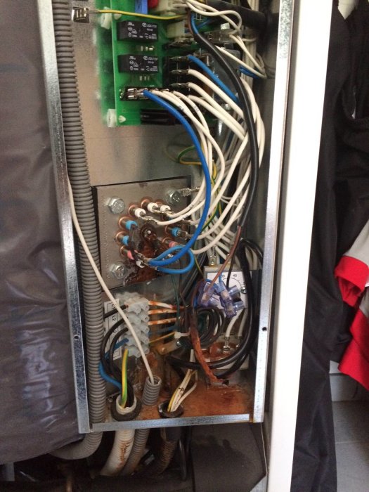 Elektriskt skåp med synlig läckage och korrosion, omgivet av kablar och komponenter.