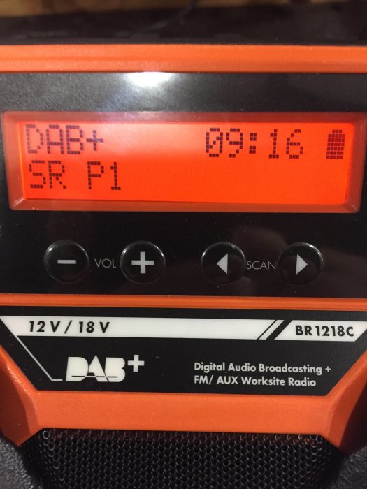 Portabel DAB+/FM-radio med digital display visande SR P1 och klockan 09:16, i orange och svart design.