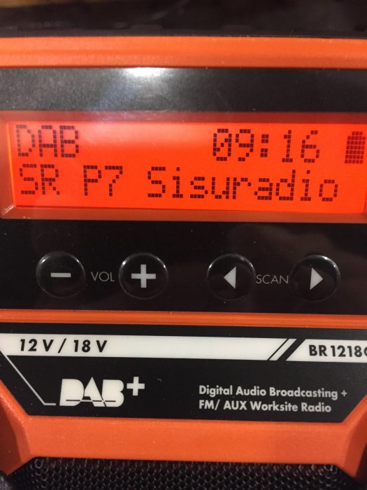 Närbild av en digital radio display visar DAB-mottagning och tid, plus styrfunktioner och logotyp.