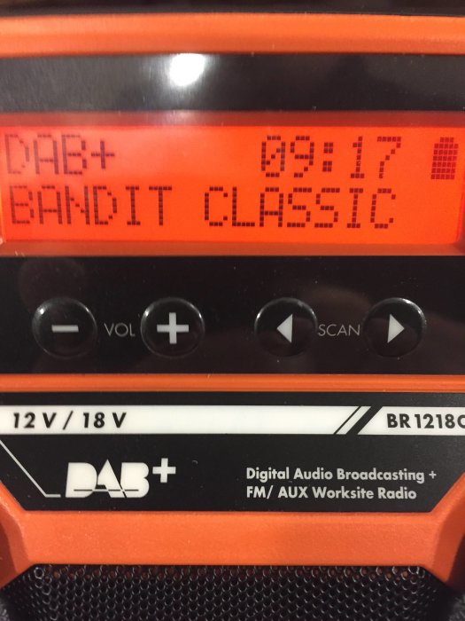 En DAB+/FM byggarbetsplatsradio med displayen visande "BANDIT CLASSIC" och kontrollknappar för volym och scanning.