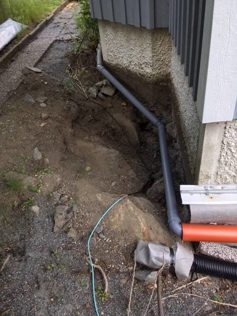 Utgrävning längs husgrund med partiellt synlig berggrund och dräneringsrör som är installerat mot husväggen.