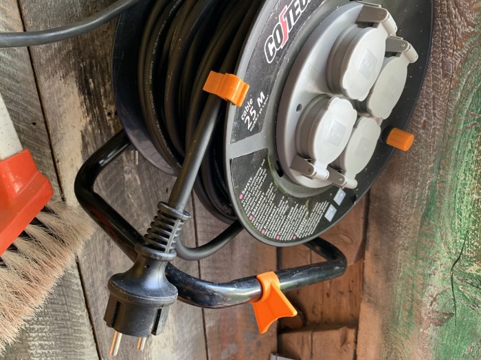 Kabelvinda med elektrisk förlängningssladd och orange plastdel för potentiellt kabelskydd.
