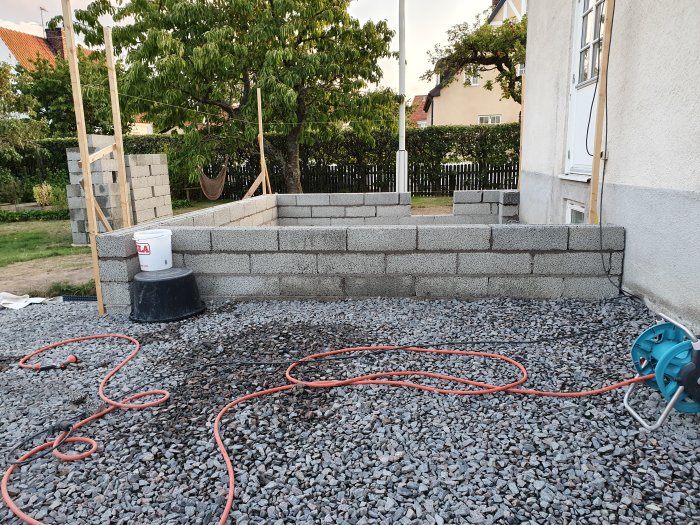 Nybyggd stödmur av grå betongblock på en terrass med grus, nära ett hus.