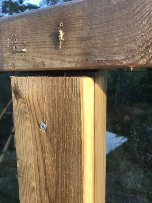 Detaljbild av trästolpe och räcke med skruvfastsättning, i förgrunden syns en del av ett glasräcke.