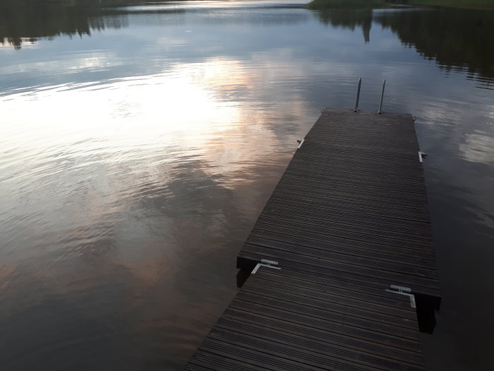 En brygga som leder ut i en stilla sjö under skymningen med speglingar av solnedgången på vattnet.