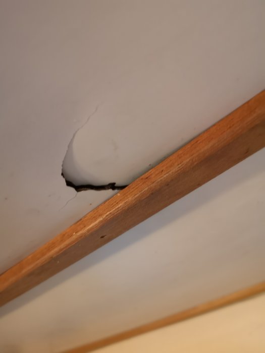 Stenhård skiva med spricka nära trälist i tak eller vägg ovan diskbänk.