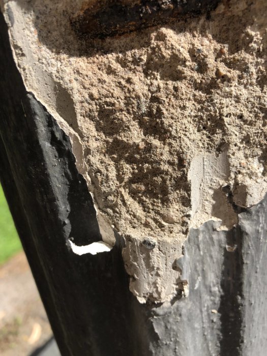 Närbild på en betongpelare med flagande svart färg och synliga skador.