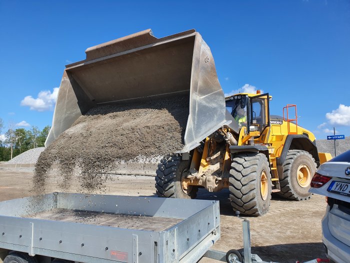 En lastmaskin av märket Volvo lämnar av grus i en släpvagn på en byggarbetsplats.